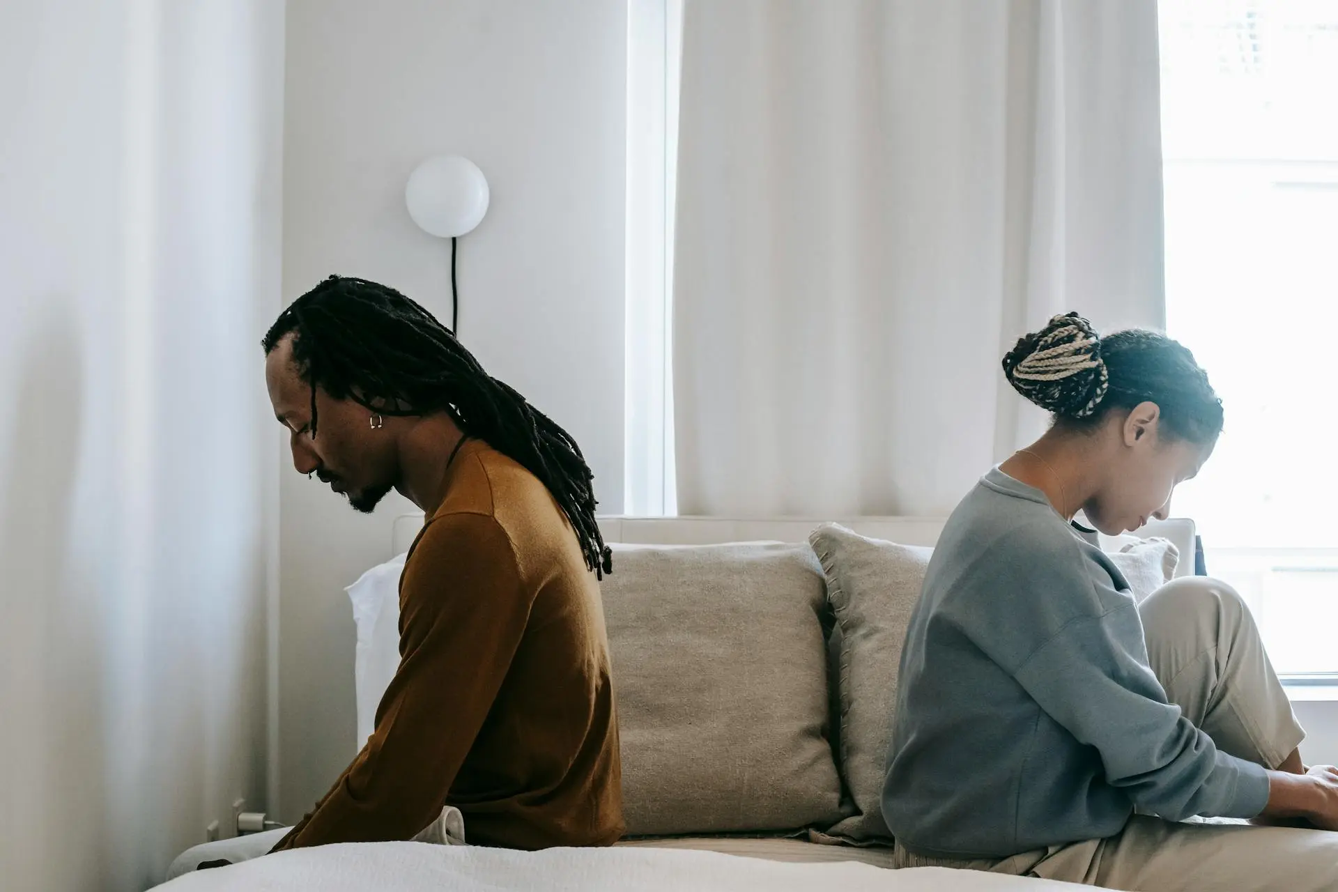 A man and woman sitting on a bed facing opposite directions