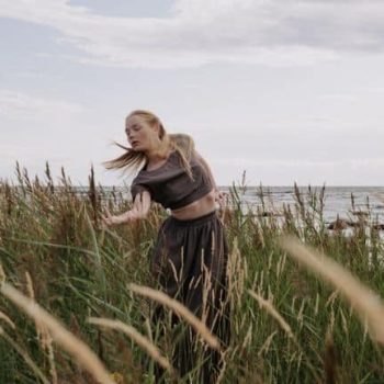 A woman is standing in tall grass near the ocean.